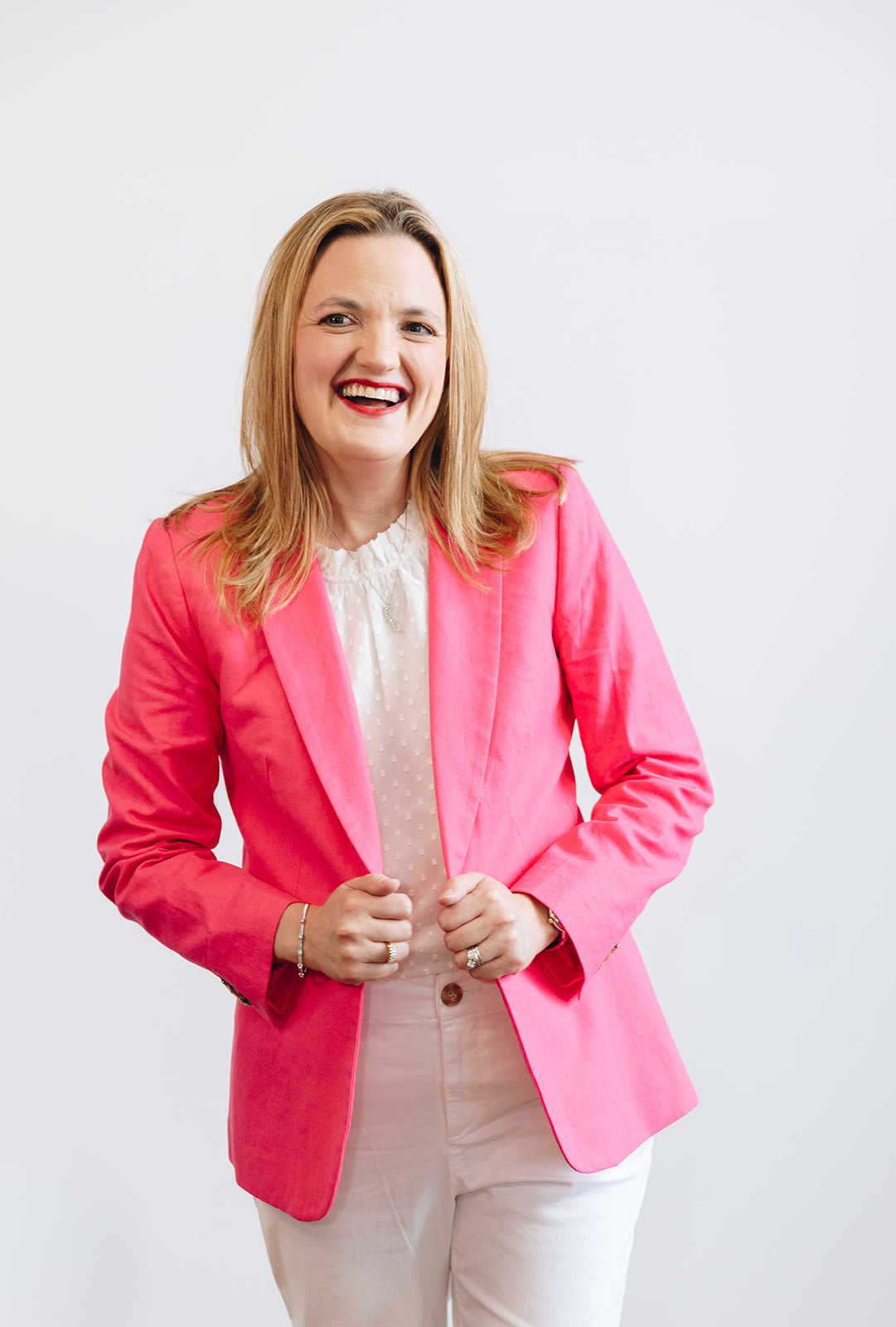 Brooke Greening, smiling and wearing a pink blazer and white blouse, standing against a plain background.